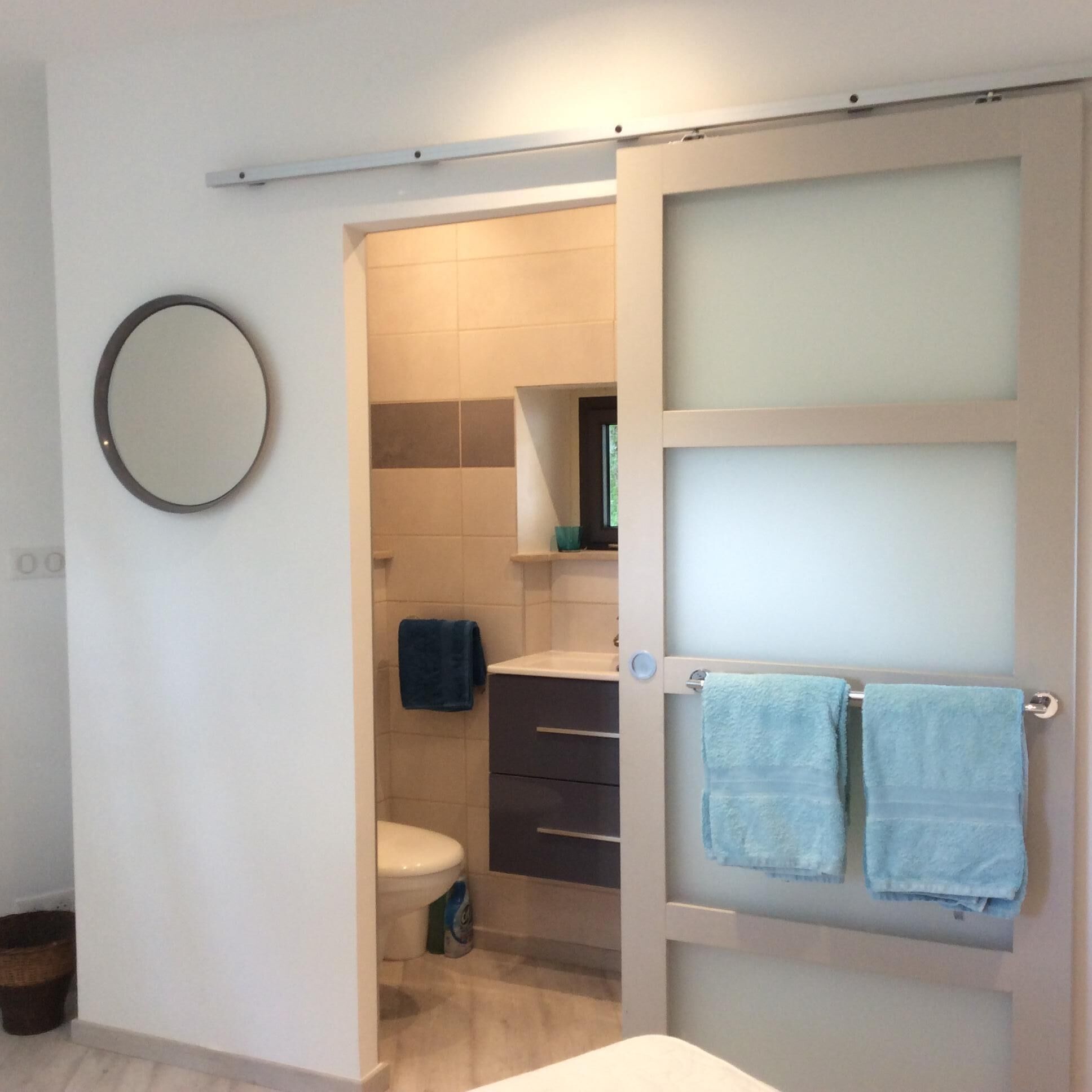 Casa de banho com sanita, lavatório, espelho e duas toalhas penduradas num porta-toalhas.