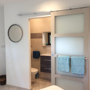 A bathroom with a toilet, a sink, a mirror, and two towels hanging on a towel rack.