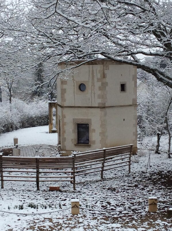 A small, two-story building with a simple, rectangular design, surrounded by snow-covered trees and a wooden fence.