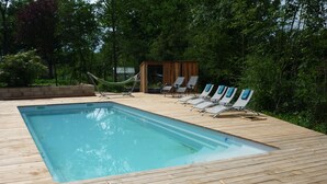 A rectangular swimming pool with a wooden deck, surrounded by lounge chairs and a hammock.