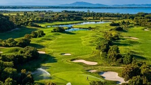 A golf course with a water body, trees, and distant mountains.