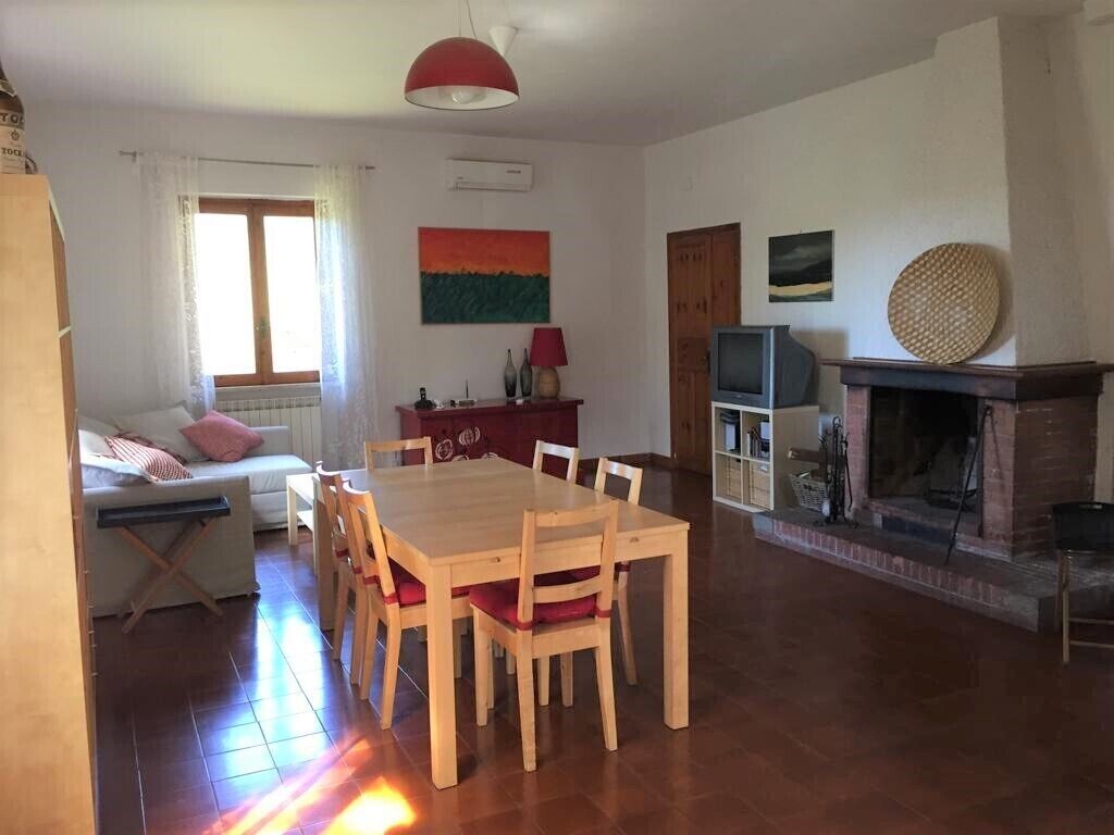 A spacious living area with a wooden dining table and chairs, a sofa, a fireplace, and a television.