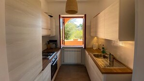 Una cocina estrecha con ventana, armarios blancos, encimera de madera y lámpara colgante.