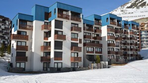 Ein mehrstöckiges Hotel mit Balkonen, im Hintergrund ein Skihang und ein klarer Himmel.