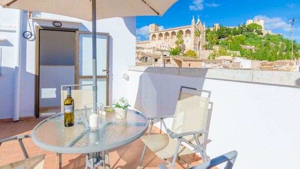 A balcony with a glass table, chairs, and an umbrella. A bottle and glasses are on the table. A door is visible in the background. - ROSER (ROSER DE ARTÀ) - Townhouse with terrace in Artà. Free WiFi (Artà)