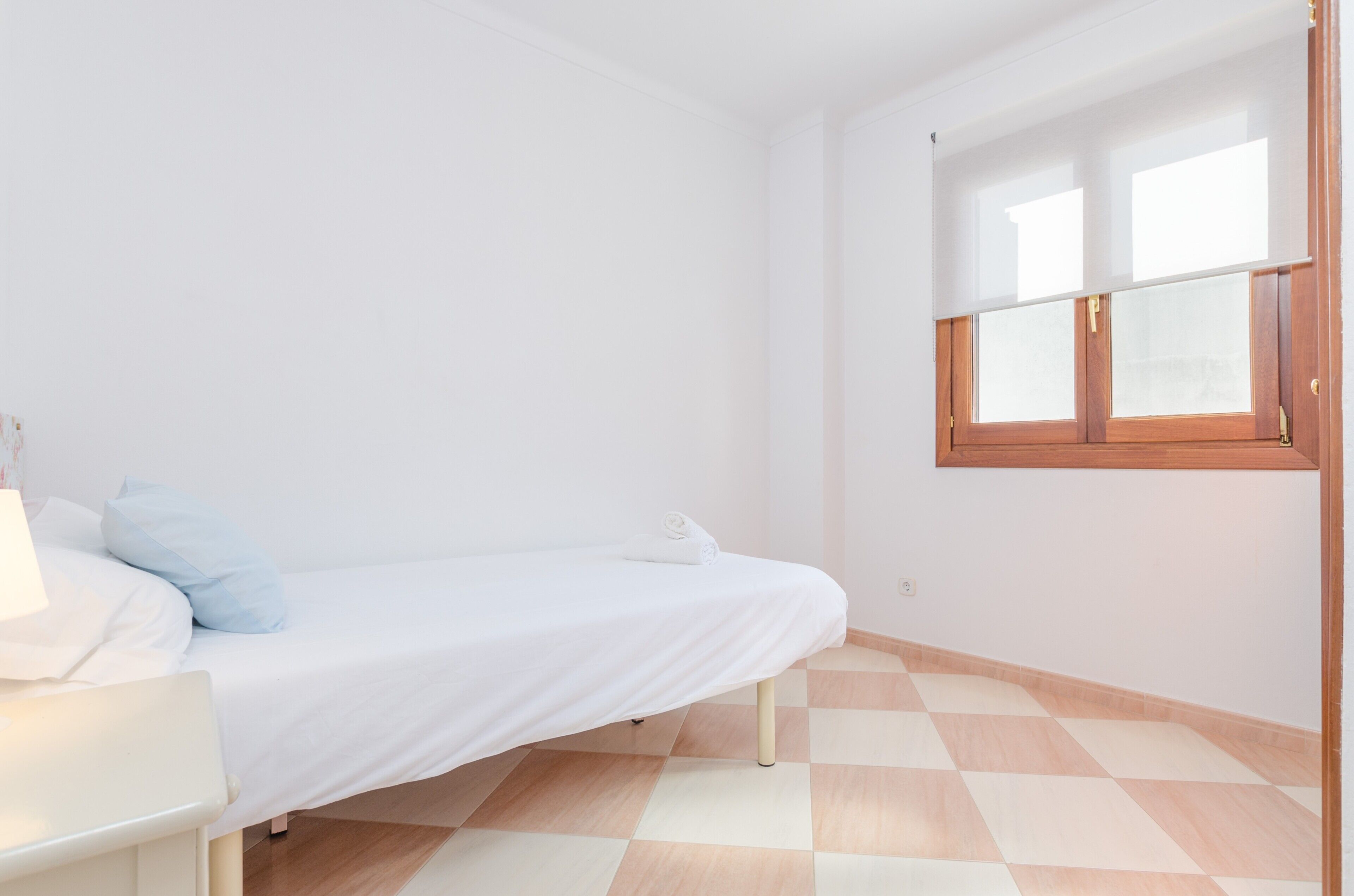 A small, clean room with a single bed, a small table, and a window with wooden shutters.