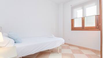 A small, clean room with a single bed, a small table, and a window with wooden shutters.