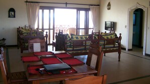 A traditional room with a wooden ceiling, a bed with a green and yellow patterned bedspread, a wooden table with red placemats, and a television on a stand. - Fantastic 3 bedroom Penthouse apartment overlooking the Indian Ocean. (Watamu)