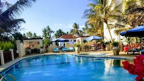 A swimming pool with lounge chairs and umbrellas, surrounded by palm trees and potted plants. - Fantastic 3 bedroom Penthouse apartment overlooking the Indian Ocean. (Watamu)