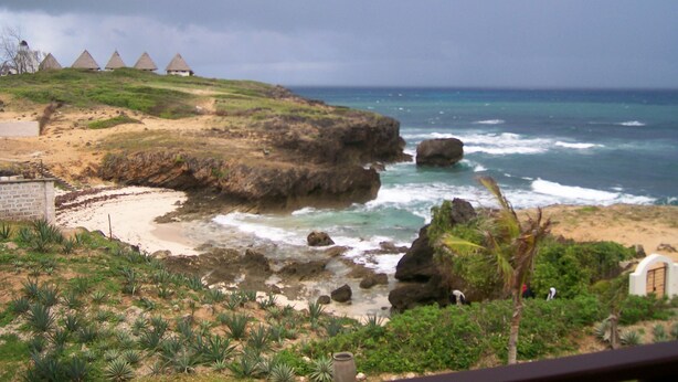 A coastal landscape with a beach, rocky outcrops, and thatched-roof huts. - Fantastic 3 bedroom Penthouse apartment overlooking the Indian Ocean. (Watamu)