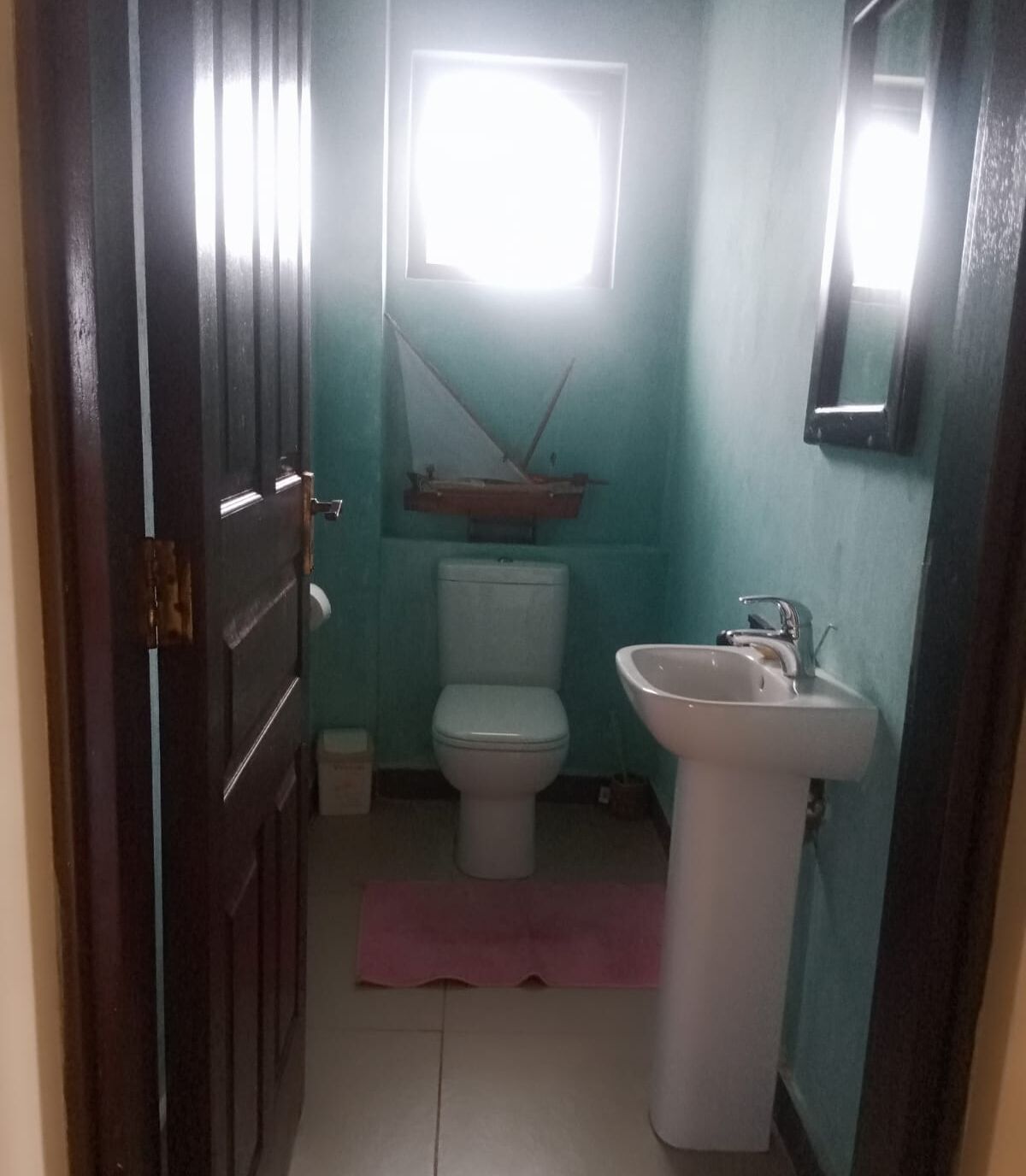 Et aflangt badeværelse med toilet, vask og et lille vindue.