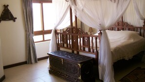 A bedroom with a four-poster bed, a wooden chest, and a window with curtains. - Fantastic 3 bedroom Penthouse apartment overlooking the Indian Ocean. (Watamu)