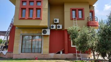 A two-story building with a red and yellow facade, multiple windows, and air conditioning units.