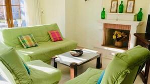 Un salon avec un canapé vert, un fauteuil assorti, une table basse et une cheminée agrémentée d’objets décoratifs.