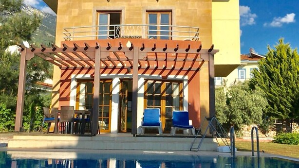 Un bâtiment à deux étages doté d’un espace piscine, comprenant une pergola avec des chaises et une table.