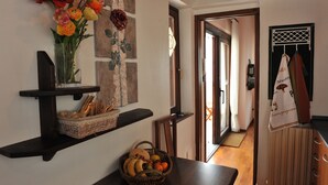 A kitchen with a wooden table, a basket of fruits, and a vase of flowers on a shelf.