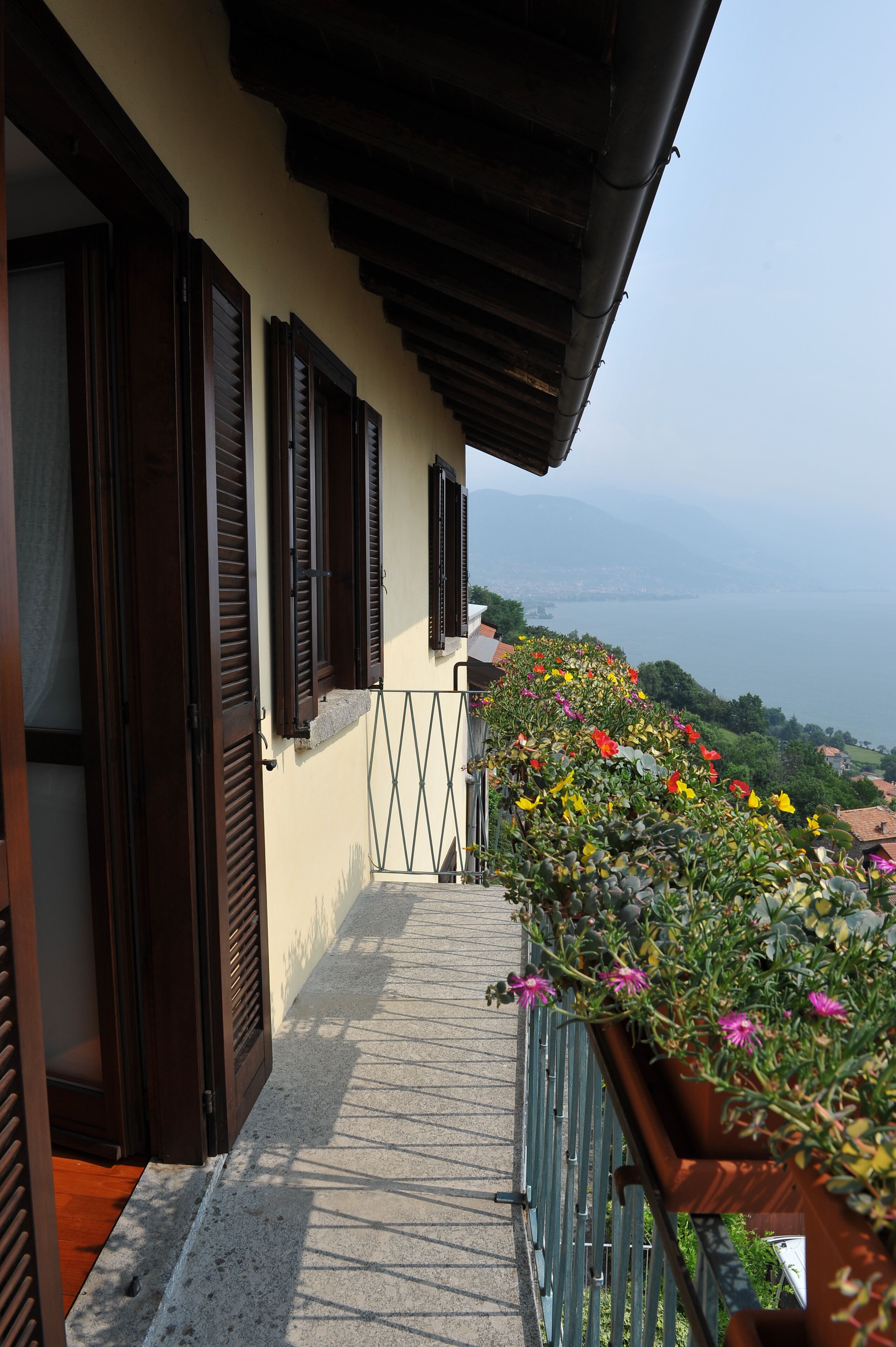 A balcony with wooden shutters, a metal railing, and a flower box with colorful flowers.
