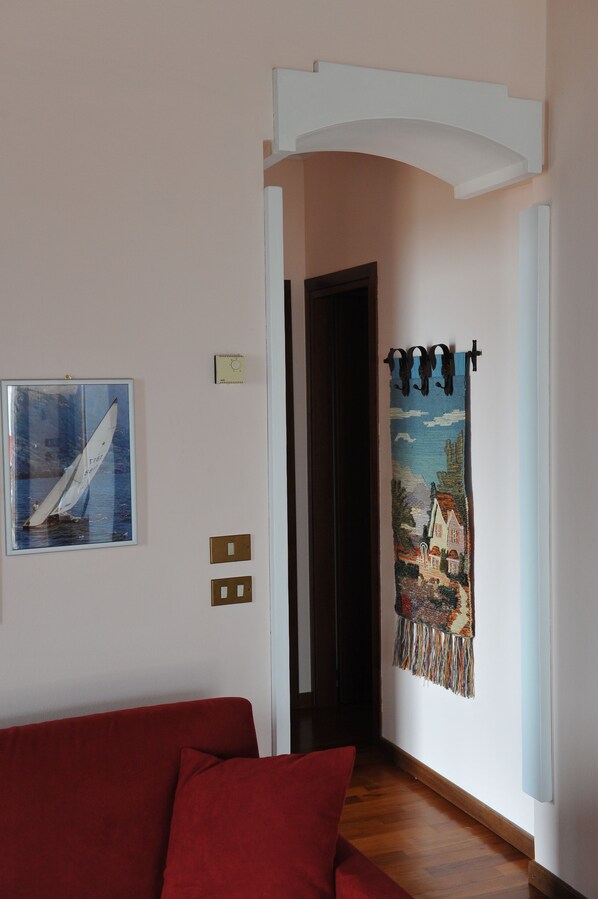 Un pasillo con un sofá rojo, un cuadro enmarcado de un velero, un tapiz y una puerta que da a otra habitación.