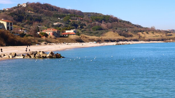 A coastal area with a sandy beach, rocky outcrops, and buildings on a hillside.