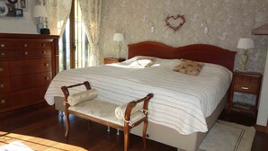 Une chambre à coucher avec un grand lit, une commode en bois, une chaise et une table de chevet avec une lampe.