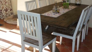 Un coin repas avec une table en bois, des chaises blanches, un chemin de table à motifs floraux, un luminaire suspendu et un tableau floral accroché au mur.