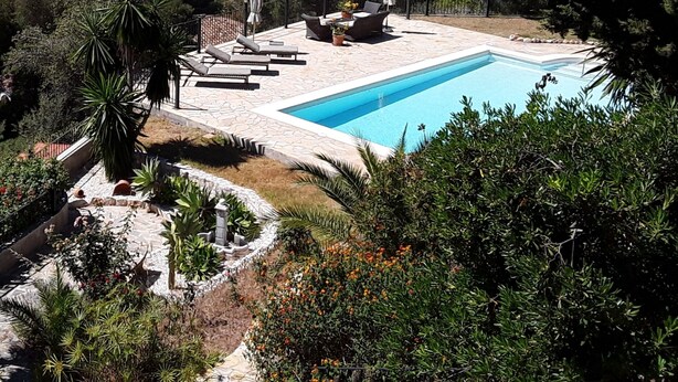 Un espace piscine agrémenté de chaises longues et de parasols, entouré de verdure et offrant une vue sur un paysage pittoresque.