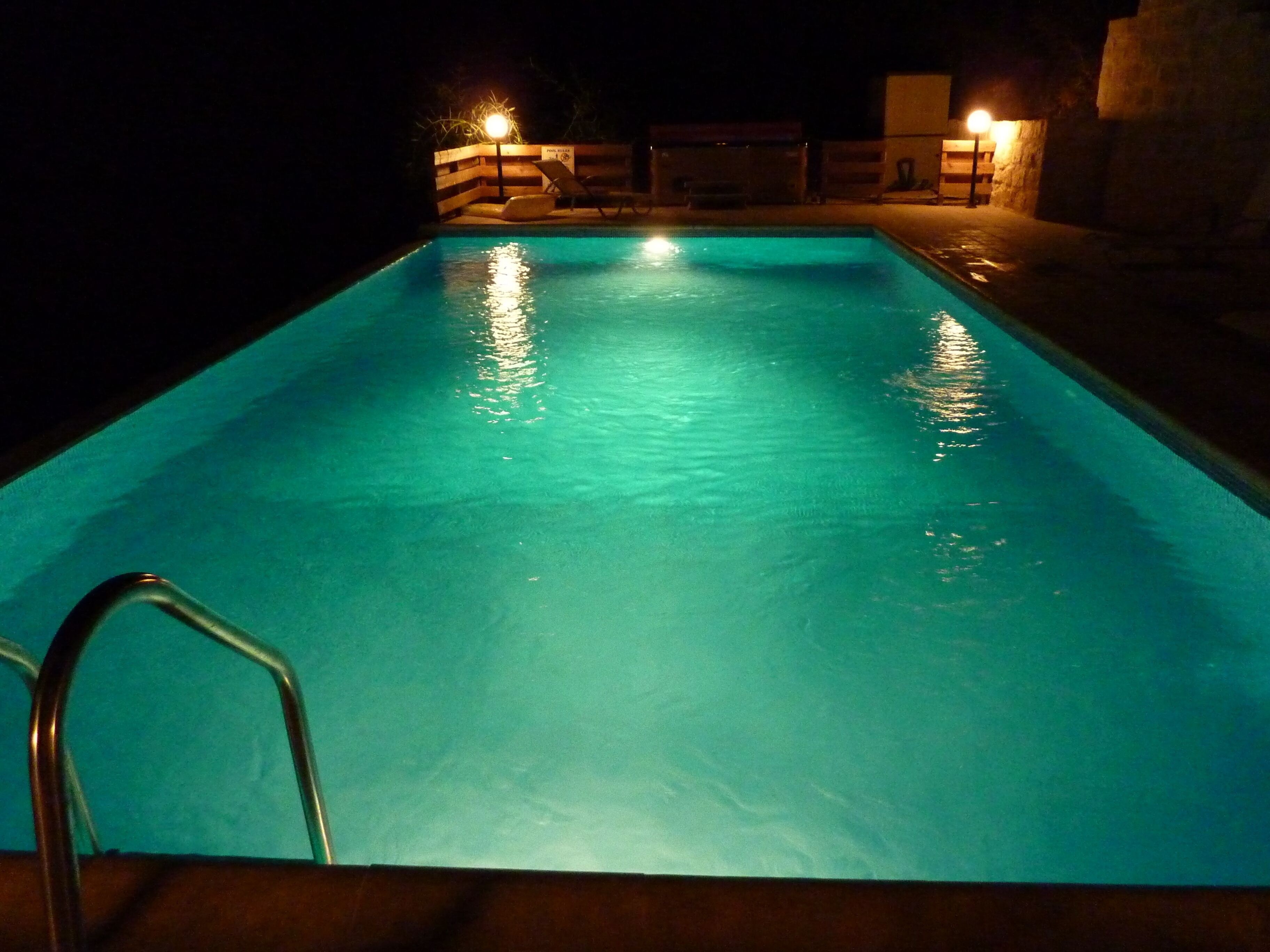 A swimming pool at night with clear water and a metal ladder.