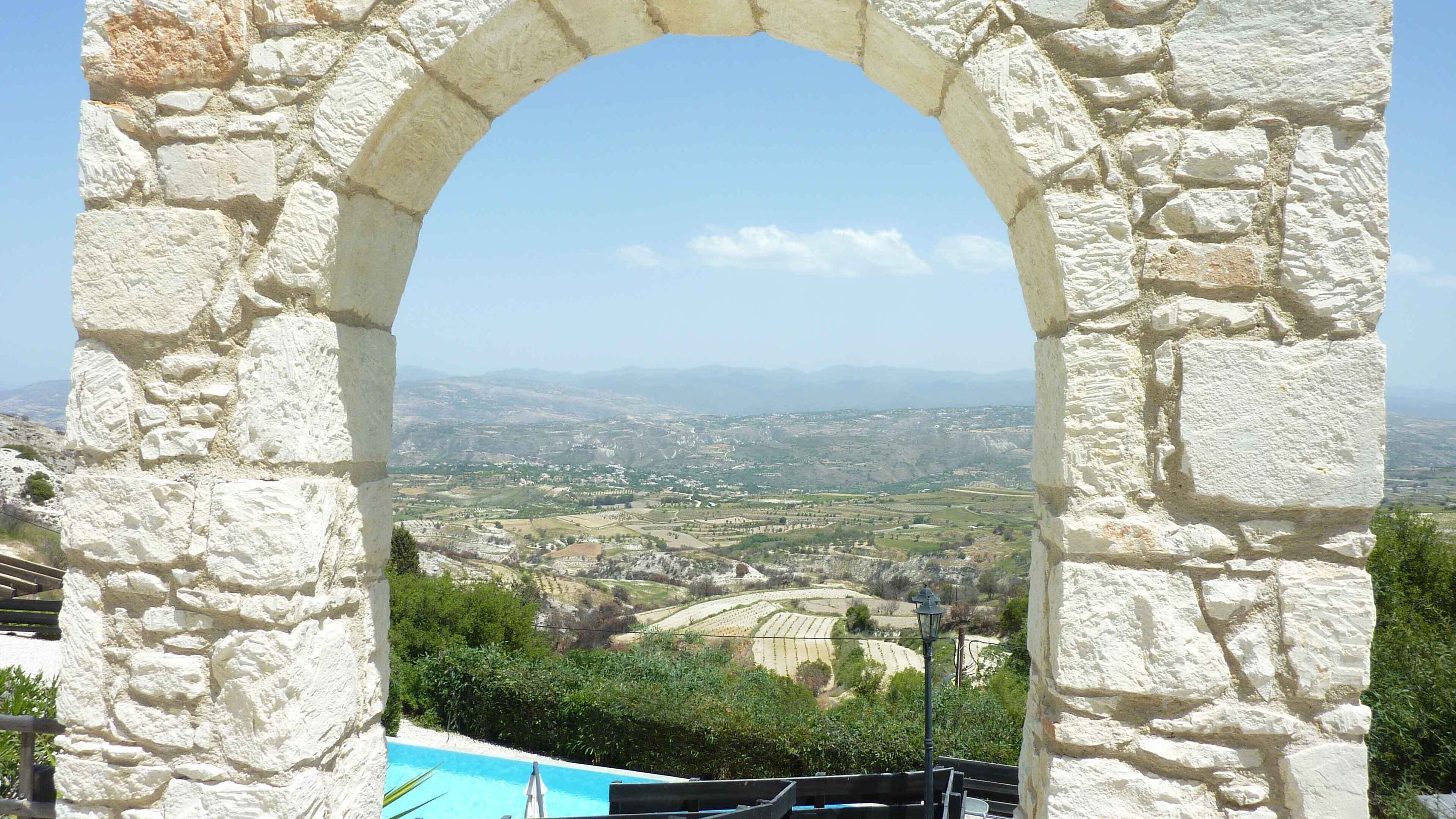 Un arc en pierre surplombe une vallée, avec une piscine et de la végétation en contrebas.