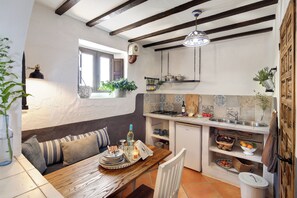 A kitchen with a wooden table, white chairs, a window, and a hanging light fixture.