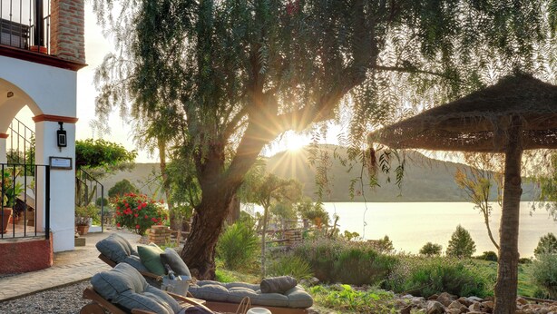 A serene outdoor seating area with lounge chairs and a thatched umbrella, overlooking a body of water and a mountainous backdrop. - Refurbished holiday apartment in an Andalusian farmhouse in The Lake District (Antequera)