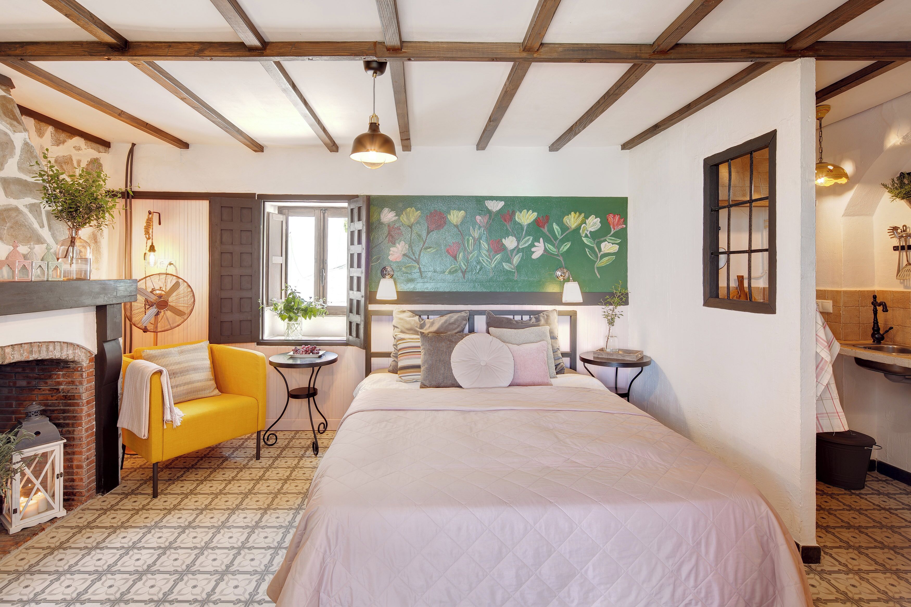Een slaapkamer met een bed, een gele fauteuil, een open haard en een groot bloemenkunstwerk aan de muur.