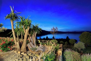 A garden with a hammock, palm trees, and a view of a lake at night.