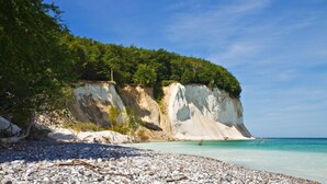 Ein Strand mit weißen Klippen, klarem türkisblauem Wasser und einem felsigen Vordergrund.