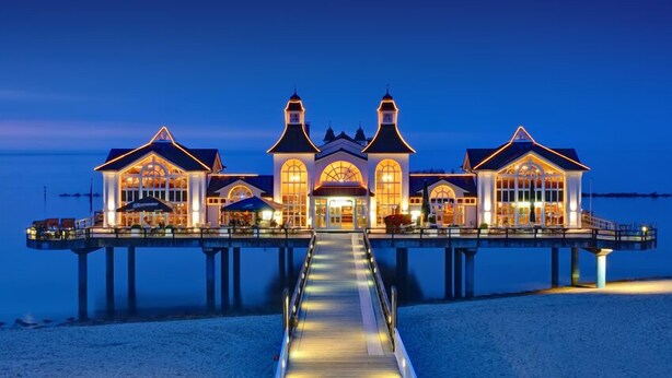 Ein Hotel am Wasserufer, mit einem zentralen Gebäude, das von zwei Türmen flankiert wird und durch einen Gang verbunden ist.