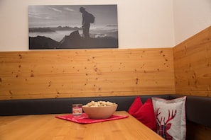 A wooden bench with a bowl of snacks and a candle, a red pillow, and a wall-mounted picture of a hiker.