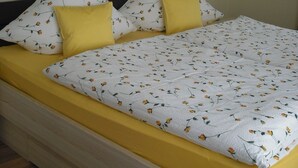 Una cama con una colcha de motivos florales y dos almohadones amarillos, un cabecero de madera y dos cuadros enmarcados en la pared.