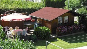 Una pequeña cabaña de madera con techo rojo, rodeada de un jardín cuidado con diversas plantas y flores.