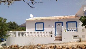 A white building with blue shutters and a satellite dish, surrounded by a white fence and rocks.