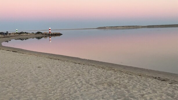 A calm beach with a lighthouse and rocky outcrops.