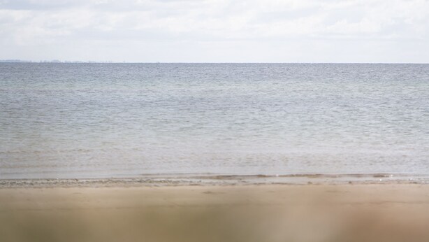 Ein Strand mit ruhiger See und bewölktem Himmel.
