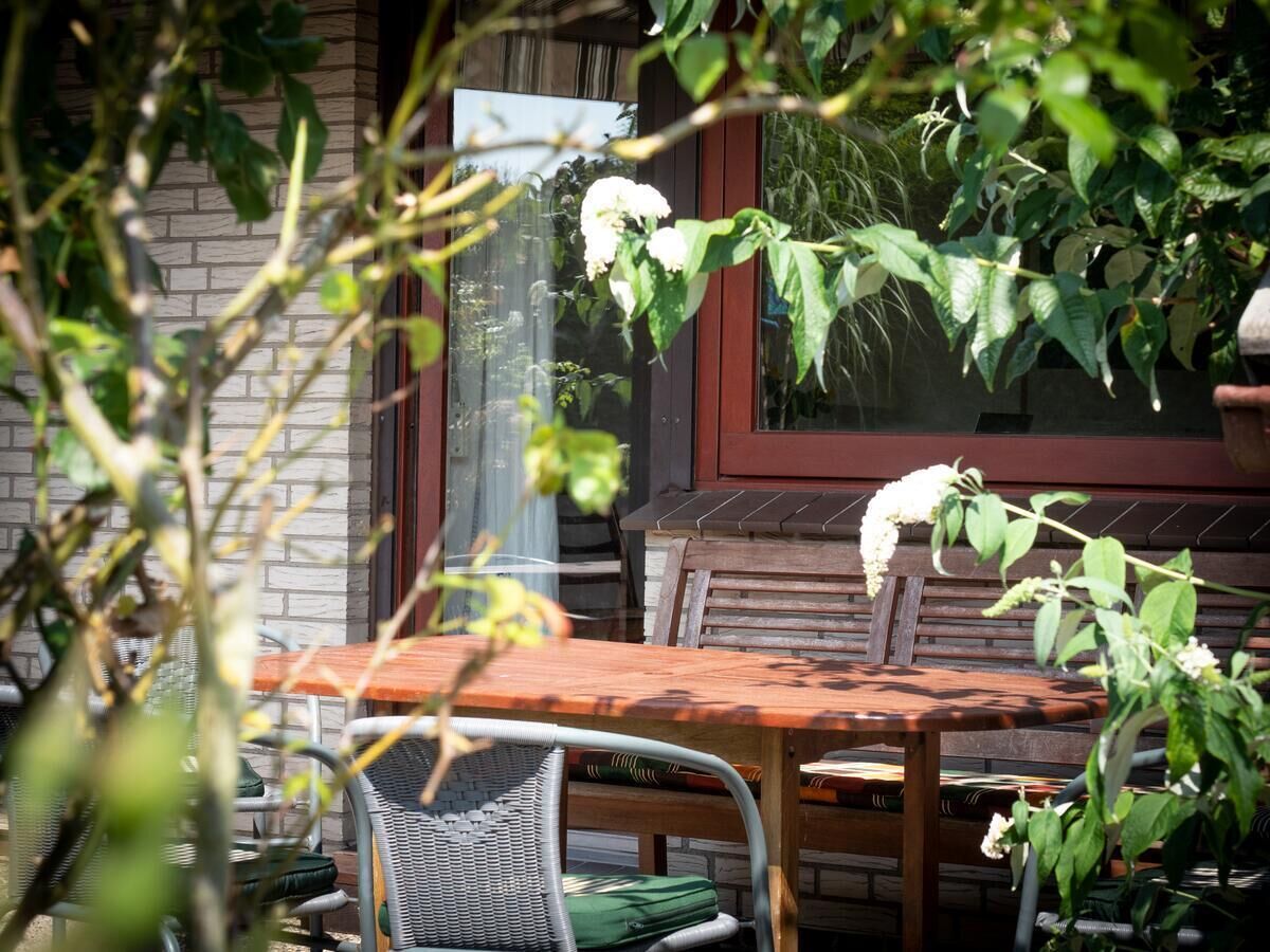 A wooden table and chairs outside a building with a brick wall and a window.