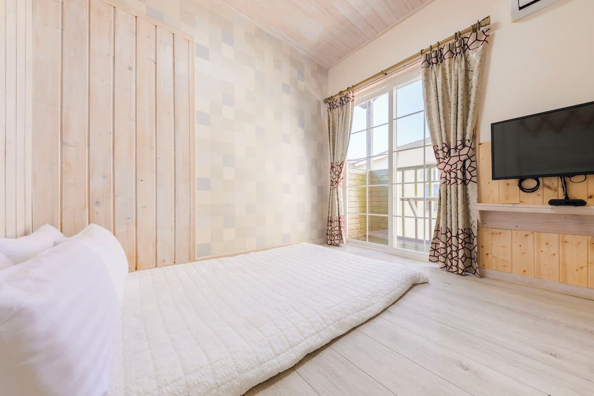 A bedroom with a bed, wooden walls, a window with curtains, and a TV on a wooden shelf.