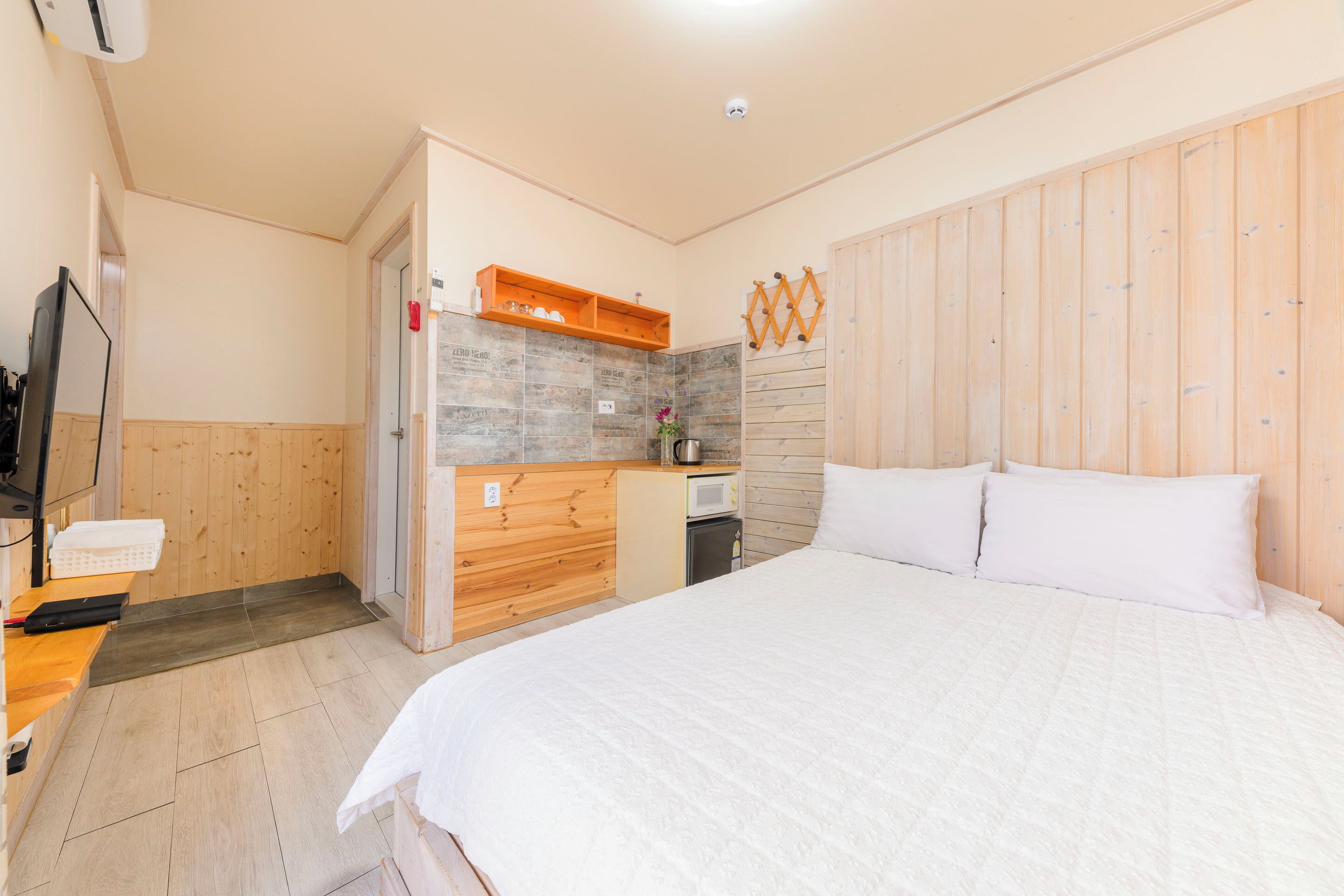 A bedroom with a large bed, wooden walls, a small kitchenette, and a TV.