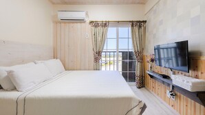 Habitación de hotel con una cama grande, un televisor sobre una estantería de madera y un balcón con cortinas.