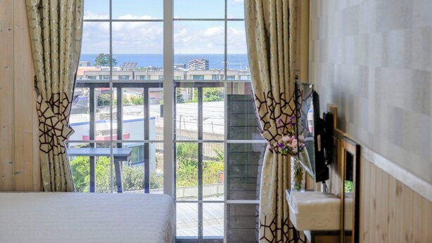 Habitación de hotel con una ventana grande, una cama, un lavamanos y vistas a la ciudad y al mar.