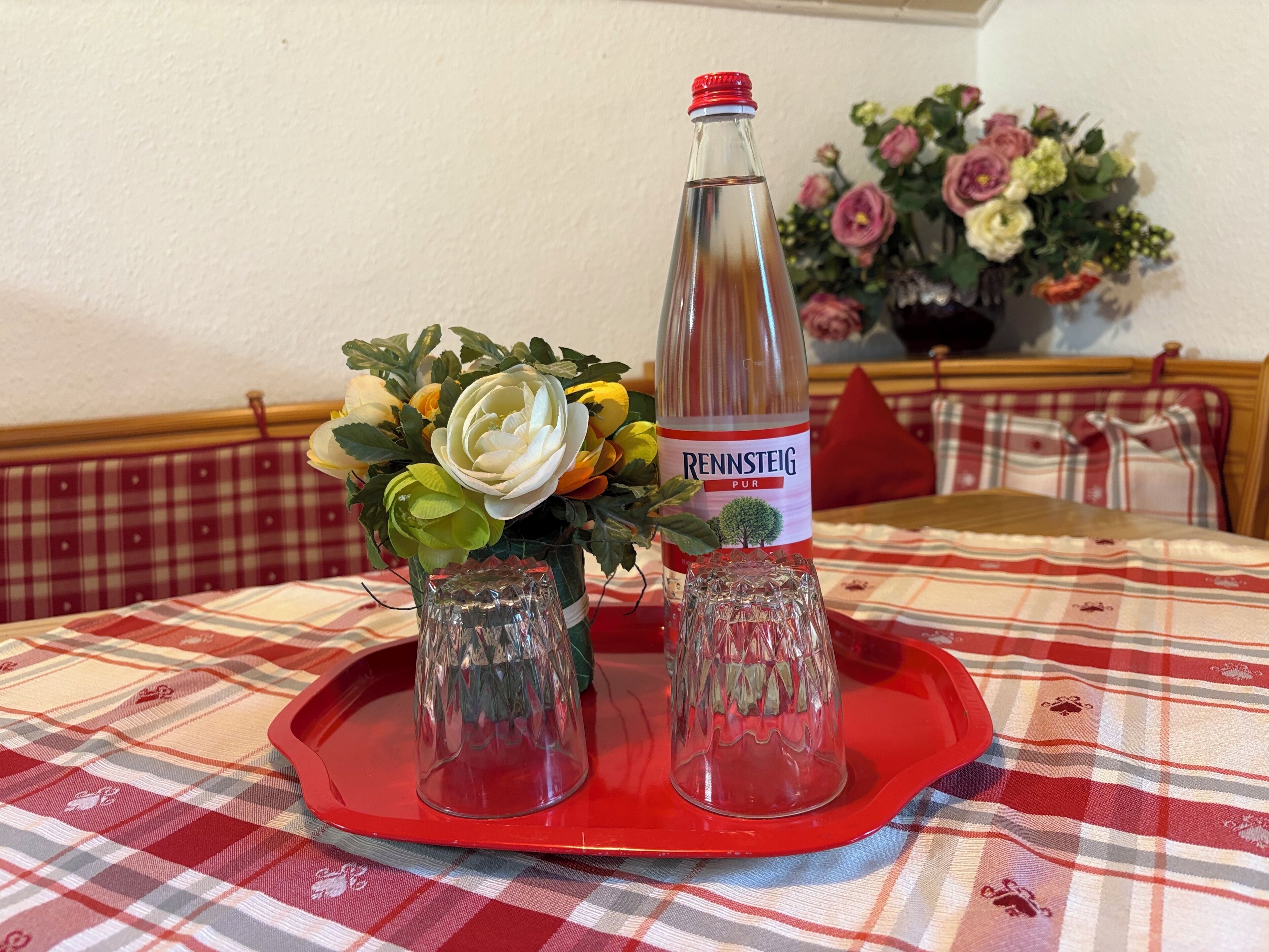 A bottle of RENNSTEIG Pur on a red tray with two glass vases containing flowers.