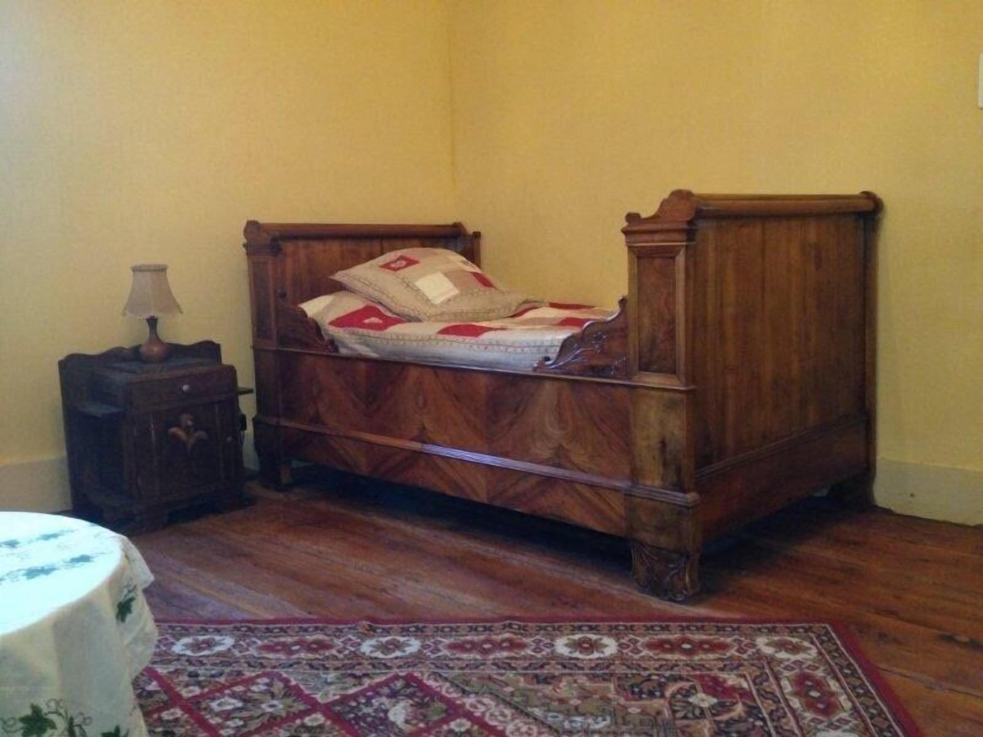 Un lit en bois avec une tête de lit, une table de chevet avec une lampe et un tapis à motifs sur un plancher en bois.