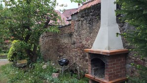 Un four extérieur en briques, doté d’une cheminée, entouré de verdure et bordé d’un mur de pierres.