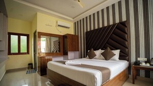 A modern hotel room with a large bed, a wooden wardrobe, a mirror, a striped wall, and a ceiling fan.