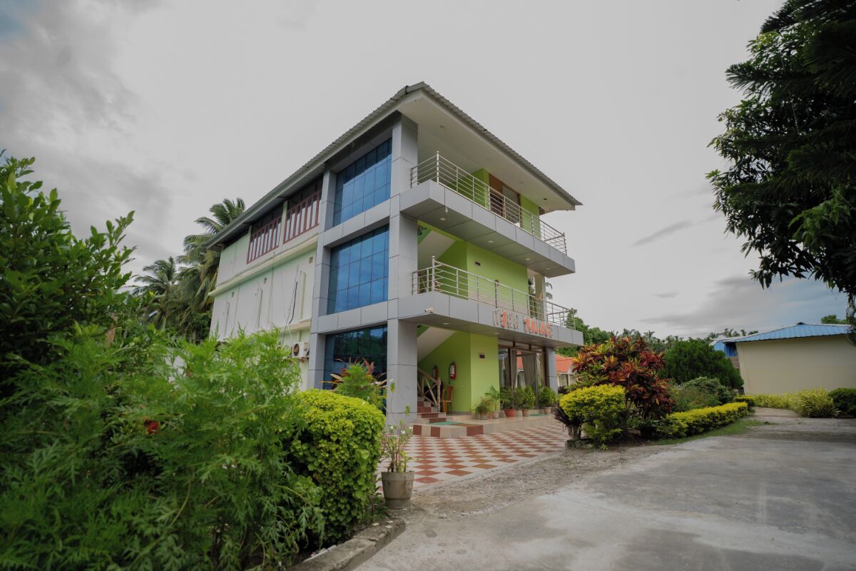 A multi-story building with a green and white facade, a balcony on the second floor, and a checkered entrance area.